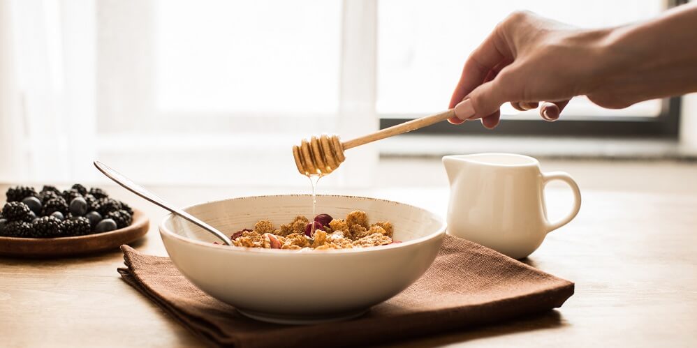 woman drizzling honey stick over oatmeal
